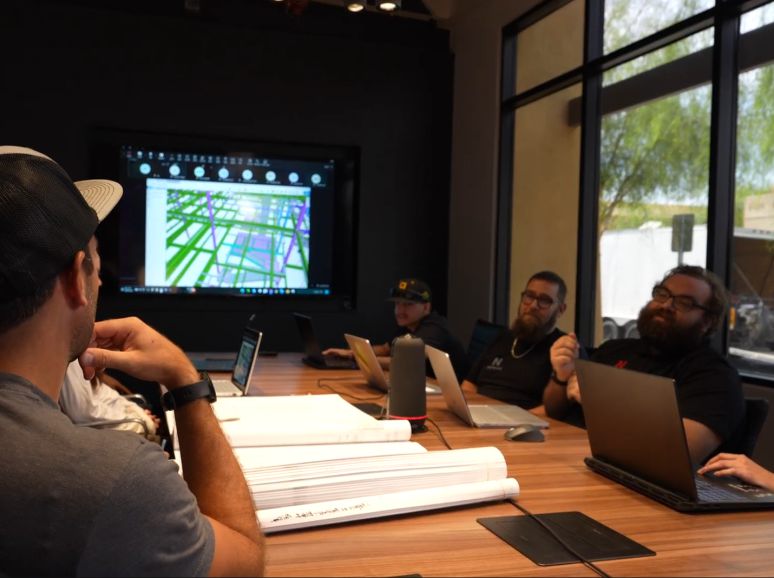 Team meeting around a table of drawings, a 3D steel model on the screen