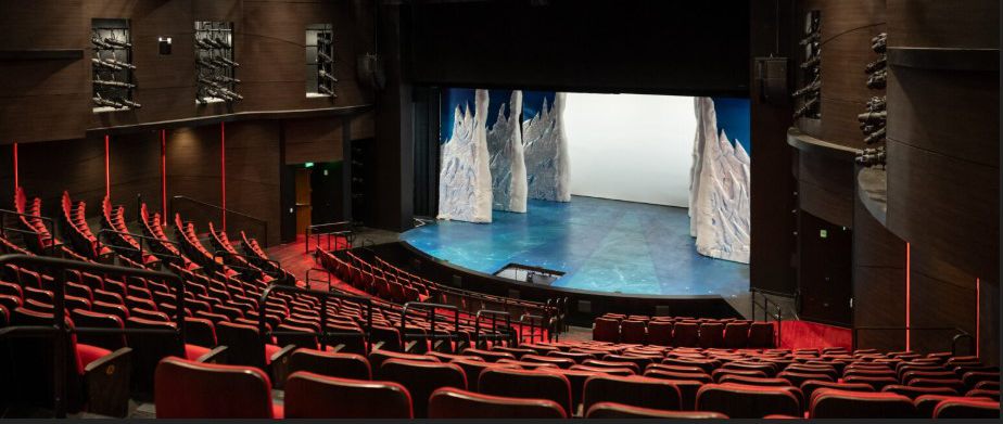 Theatre auditorium with red seats facing a lit stage