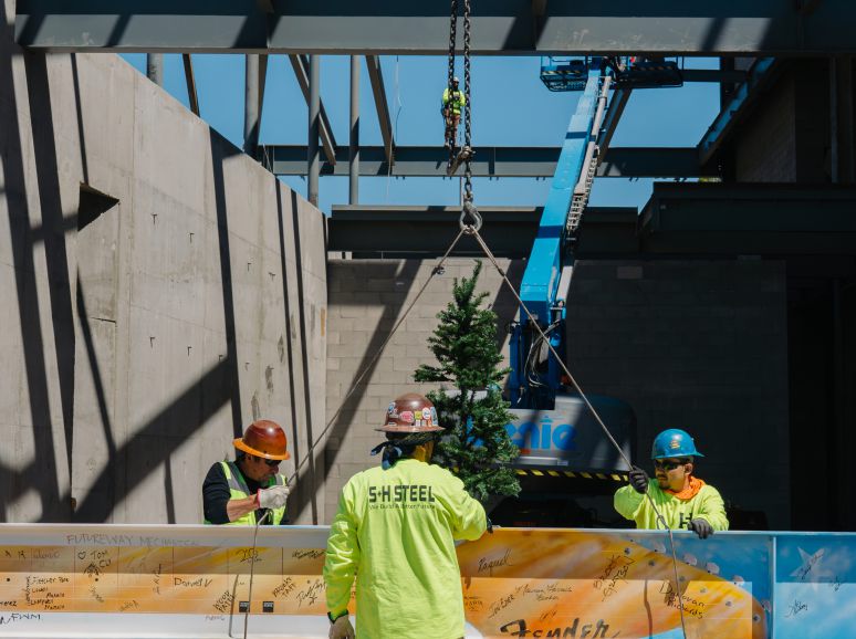 Crew in safety vests guiding a painted steel beam under a crane