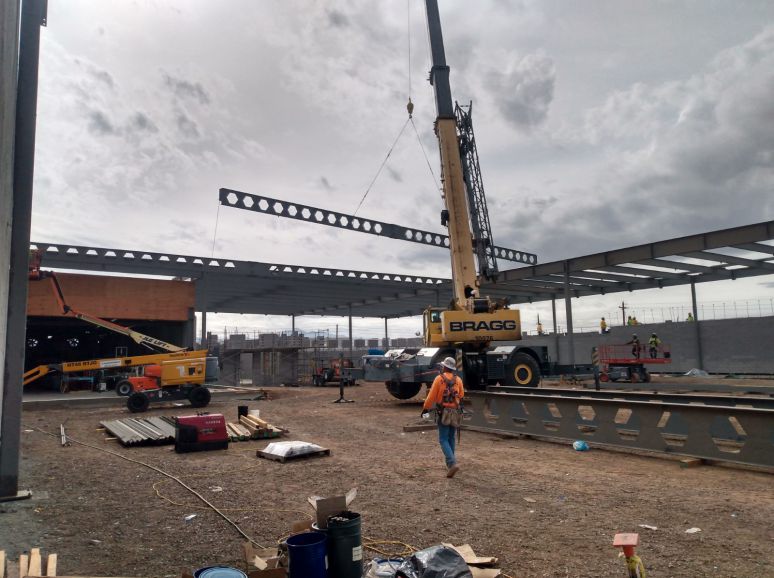 Crane lifting a steel truss on an open site